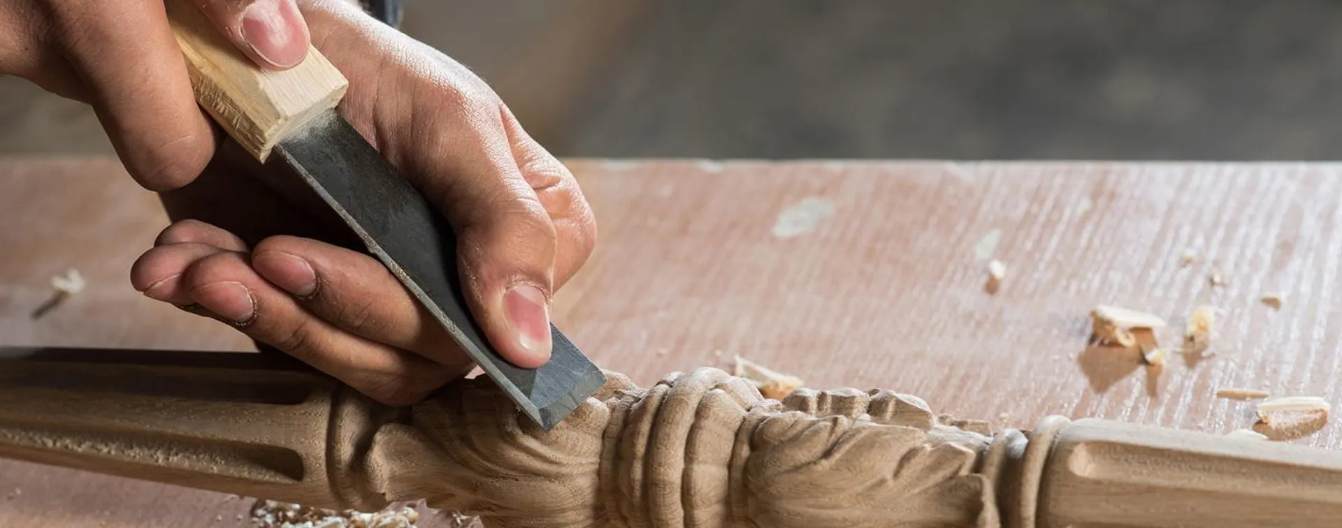 Hände führen ein Stecheisen über ein Werkstück aus Holz